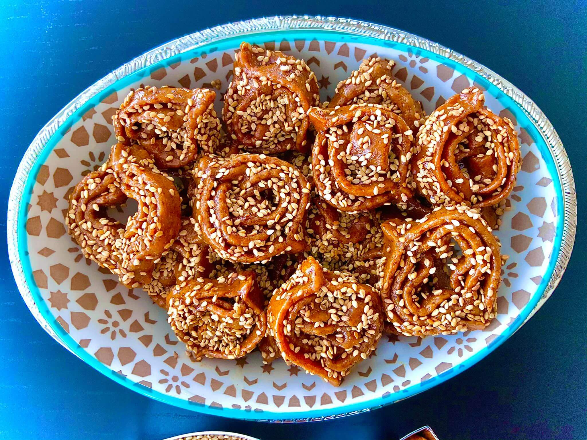 A plate of golden Moroccan Chebakia, featuring intricately twisted deep-fried pastries drizzled with honey and sprinkled with sesame seeds, served warm for a sweet and aromatic treat.